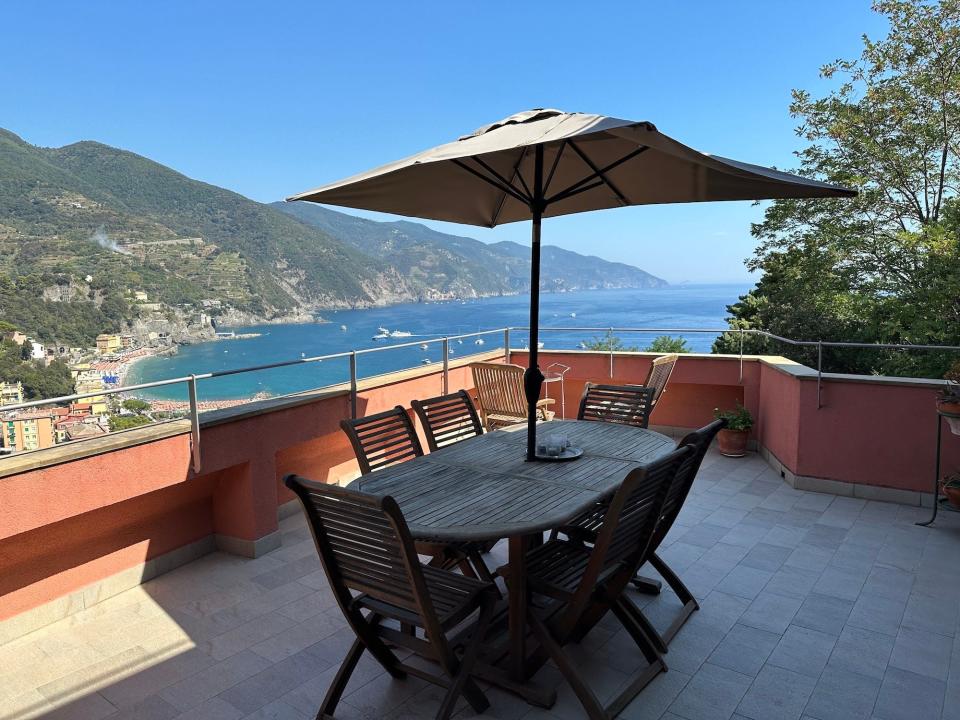 A patio with a large table and umbrella and views of the ocean.