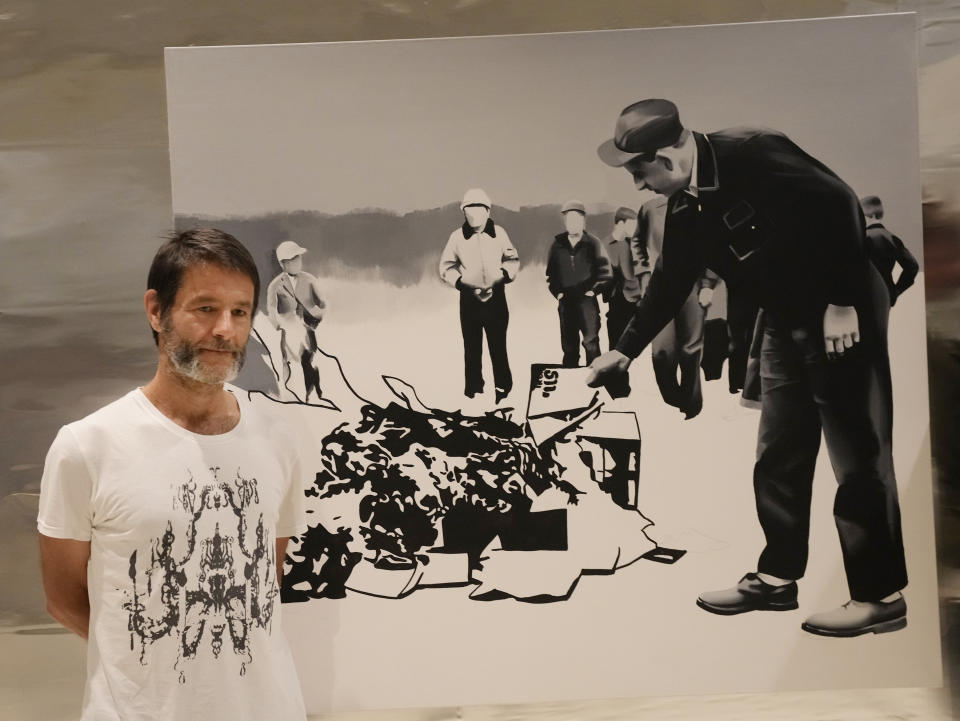 Polish artist Wilhelm Sasnal poses in front of one of his art works on display in a new exhibition at the POLIN Museum of the History of Polish Jews, in Warsaw, Poland, on Tuesday June 15, 2021. "Wilhem Sasnal: Such a Landscape" opened Thursday. The dozens of paintings and drawings on display confront the Holocaust in the nation's physical and mental landscape and the difficulty in Poland in addressing an unsettled past.(AP Photo/Czarek Sokolowski)