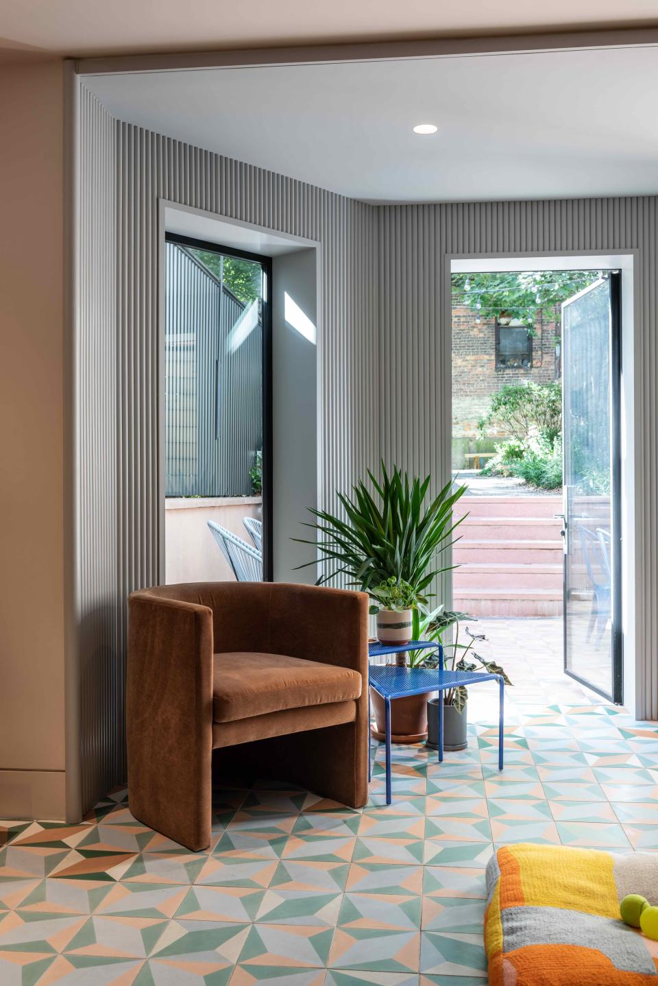 “One of the main draws of this house was the backyard—it’s unusually big for Brooklyn,” says Michael. The ceramic tile extends outdoors, leading up to a garden and lawn. An ARC Armchair by TRNK frames the back entryway.