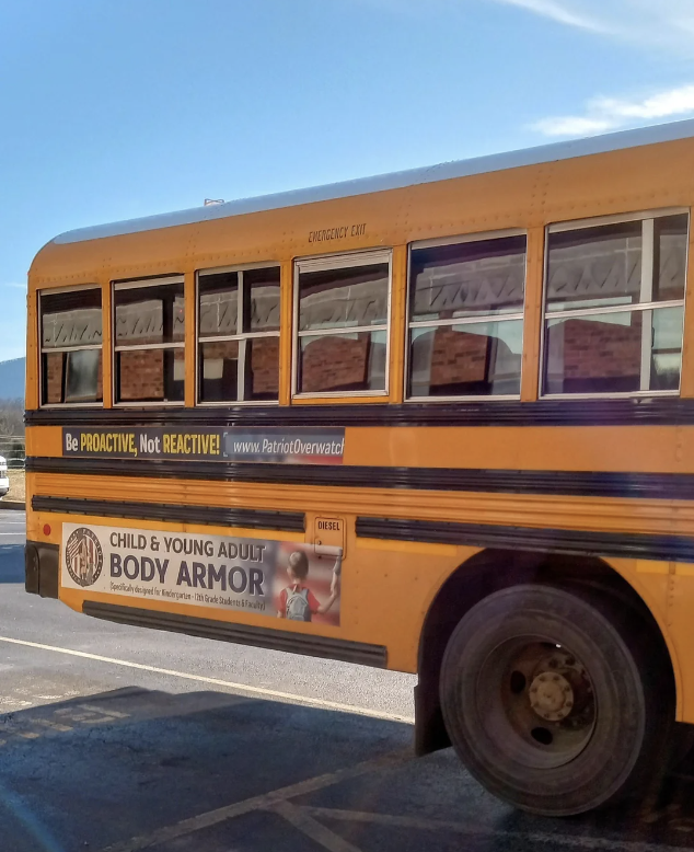 Side view of a yellow school bus with two advertisements; one reads "Be PROACTIVE, Not REACTIVE!" while another promotes child and young adult body armor