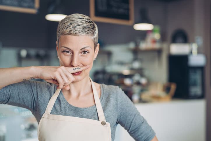 Woman posing with a playful mustache gesture in a cafe setting