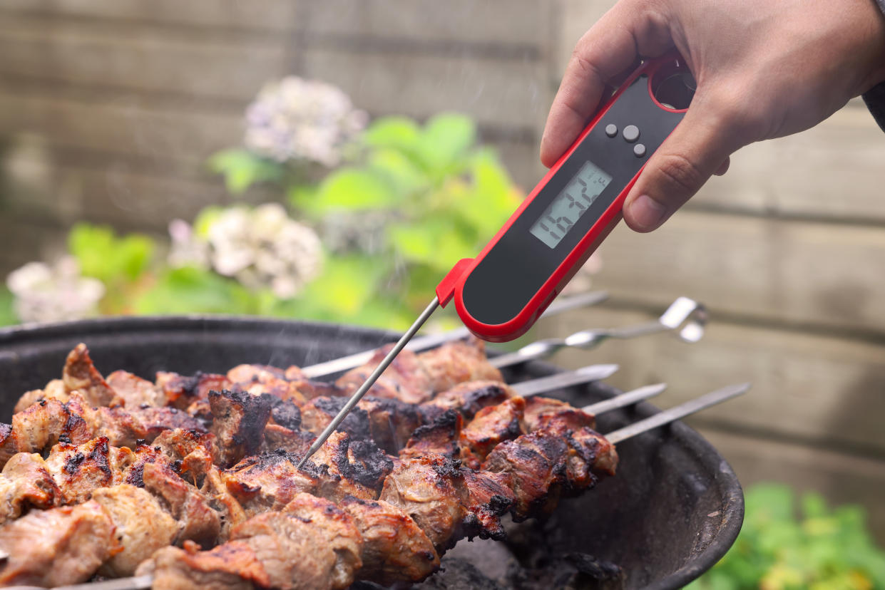 Man measuring temperature of delicious kebab on metal brazier outdoors, closeup