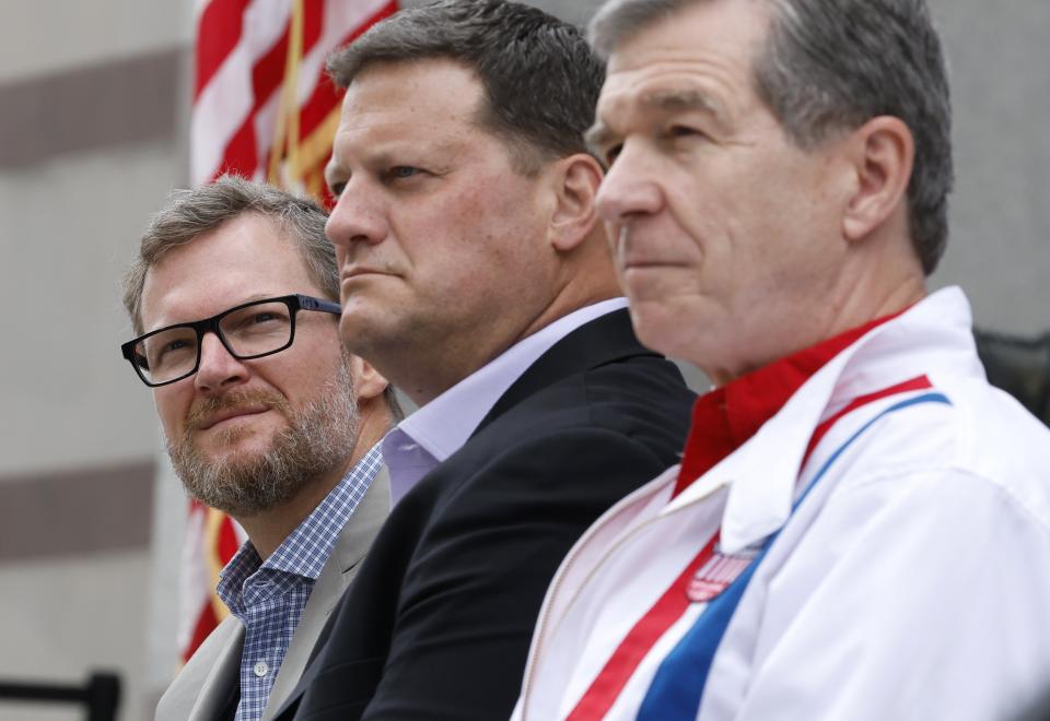 From left, Dale Earnhardt Jr., NASCAR Chief Operating Officer Steve O'Donnell and N.C. Governor Roy Cooper listen as Speedway Motorsports President and CEO Marcus Smith speaks during a press conference announcing that the NASCAR All-Star Race will be held at North Wilkesboro Speedway in May 2023. The press conference was held on the steps of the N.C. Museum of History in Raleigh, N.C., Thursday, Sept. 8, 2022. (Ethan Hyman/The News & Observer via AP)