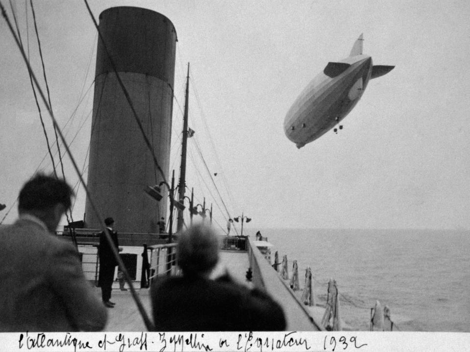 Passengers aboard a ship below watch a zeppelin crossing the Atlantic Ocean in 1932.