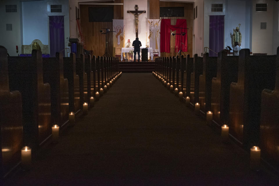 FILE - In this April 11, 2020, file photo, a person films pastor Nicolas Sanchez, center left, celebrating Easter Vigil Mass at his church decorated with candles and pictures sent by his parishioners attached to their pews at St. Patrick Church in North Hollywood, Calif. The Friday, May 22 anticipated release of new federal guidance on resuming in-person religious services during the pandemic comes ahead of a week that was already poised to rattle what’s been a weeks-long national balancing act – pitting the call to worship against the risk of the coronavirus.(AP Photo/Damian Dovarganes, File)