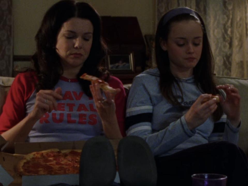 lorelai and rory sitting on the couch eating pizza on gilmore girls