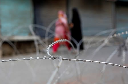 Kashmiri women walk past concertina wire laid across a road during restrictions after the scrapping of the special constitutional status for Kashmir by the Indian government, in Srinagar