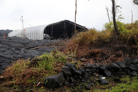 With a destroyed structure in the background, a man-made lava rock wall sits across from the Kilauea lava flow that cut through Leilani Estates near Pahoa, Hawaii, U.S., May 29, 2018. REUTERS/Marco Garcia