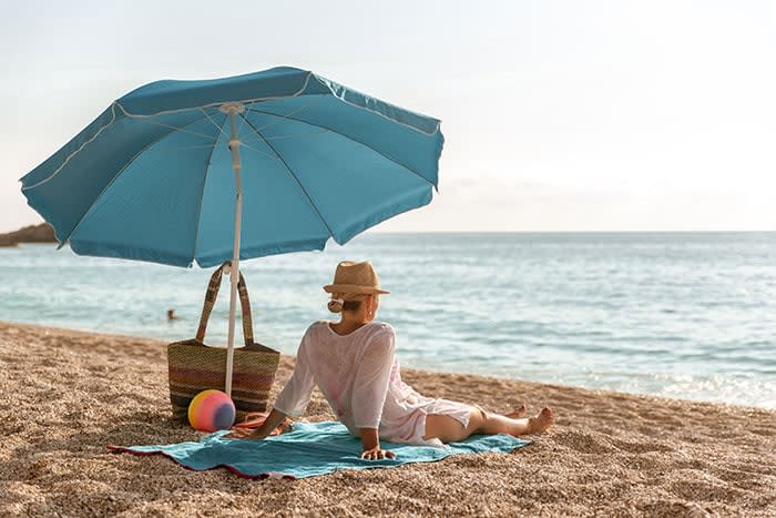 mujer protegiéndose del sol en la playa con una sombrilla