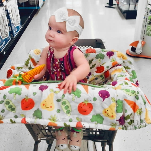 A baby in a shopping cart with the cover on it