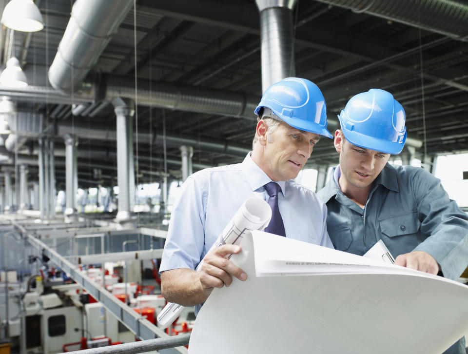 Two men looking at blueprints with an industrial facility in the background