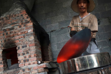 A blacksmith works on a wok at a workshop for handmade woks in Datian village, Hubei province, China August 13, 2018. REUTERS/Thomas Suen