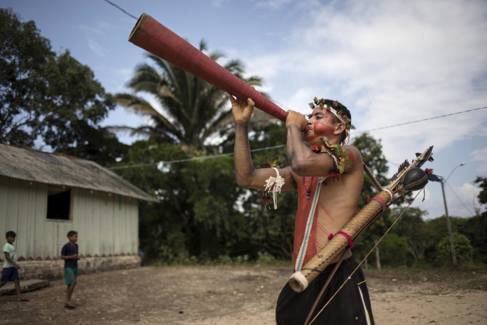 In this Sept. 3, 2019 photo, a man plays a horn during a meeting of Tembé tribes in Tekohaw indigenous reserve, Para state, Brazil. Under a thatch-roof shelter in the Amazon rainforest, warriors wielding bows and arrows, elderly chieftains in face paint and nursing mothers gathered to debate a plan that some hope will hold at bay the loggers and other invaders threatening the tribes of the Tembe. (AP Photo/Rodrigo Abd)