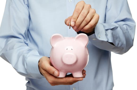 Male hand putting coin into a piggy bank.