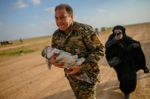 A member of the Kurdish-led Syrian Democratic Forces (SDF) carries a baby followed by a woman who fled the Islamic State (IS) group's last holdout of Baghouz, in northern Syria's Deir Ezzor province