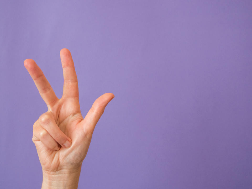 Hand with three fingers raised on purple background and copy space