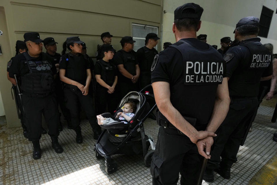 A passerby pushes baby stroller past police guarding the polling station where presidential candidate Javier Milei will vote in the presidential runoff election in Buenos Aires, Argentina, Sunday, Nov. 19, 2023. (AP Photo/Matias Delacroix)