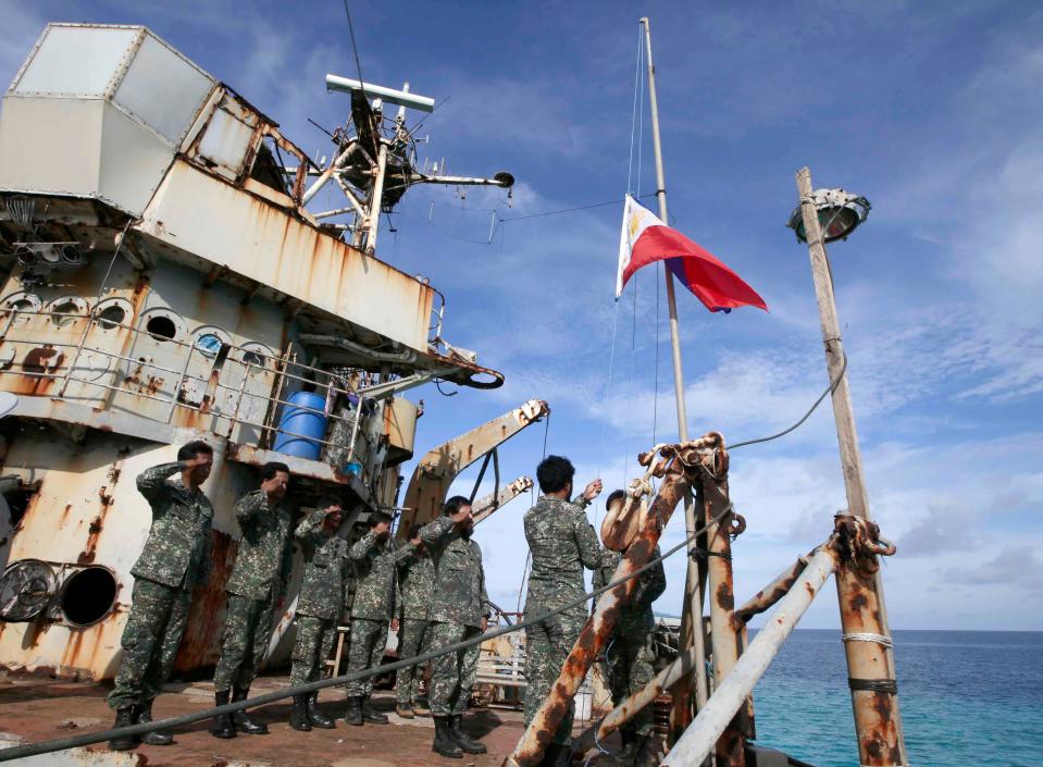 A photo of Philippine marines raising the flag on the BRP Sierra Madre while others salute.