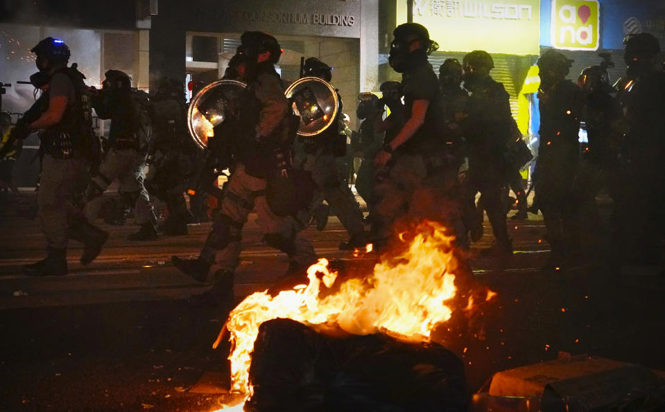 Police in full gear pass burning debris as they walk the streets during a protest in Hong Kong, Saturday, Nov. 2, 2019. Riot police fired multiple rounds of tear gas and used water cannons Saturday to swiftly break up a rally in downtown Hong Kong by thousands of masked protesters demanding meaningful autonomy after Beijing indicated it could tighten its grip on the Chinese territory. (AP Photo/Vincent Yu)