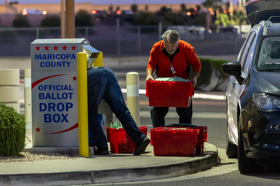 Election workers remove ballots from a drop box.