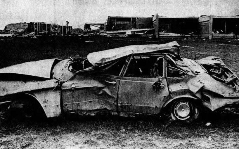 Crumpled by the force of whirling winds, this car was hurled from the Monroe Central parking lot into the lawn area adjacent to the school after a tornado touched down in Randolph County at Ind. 32 and County Road 1000-W about 3:30 p.m. on April 3, 1974. In the background, the ruins of the Monroe Central school stand in mute evidence to the force of the mighty winds. The school was demolished.