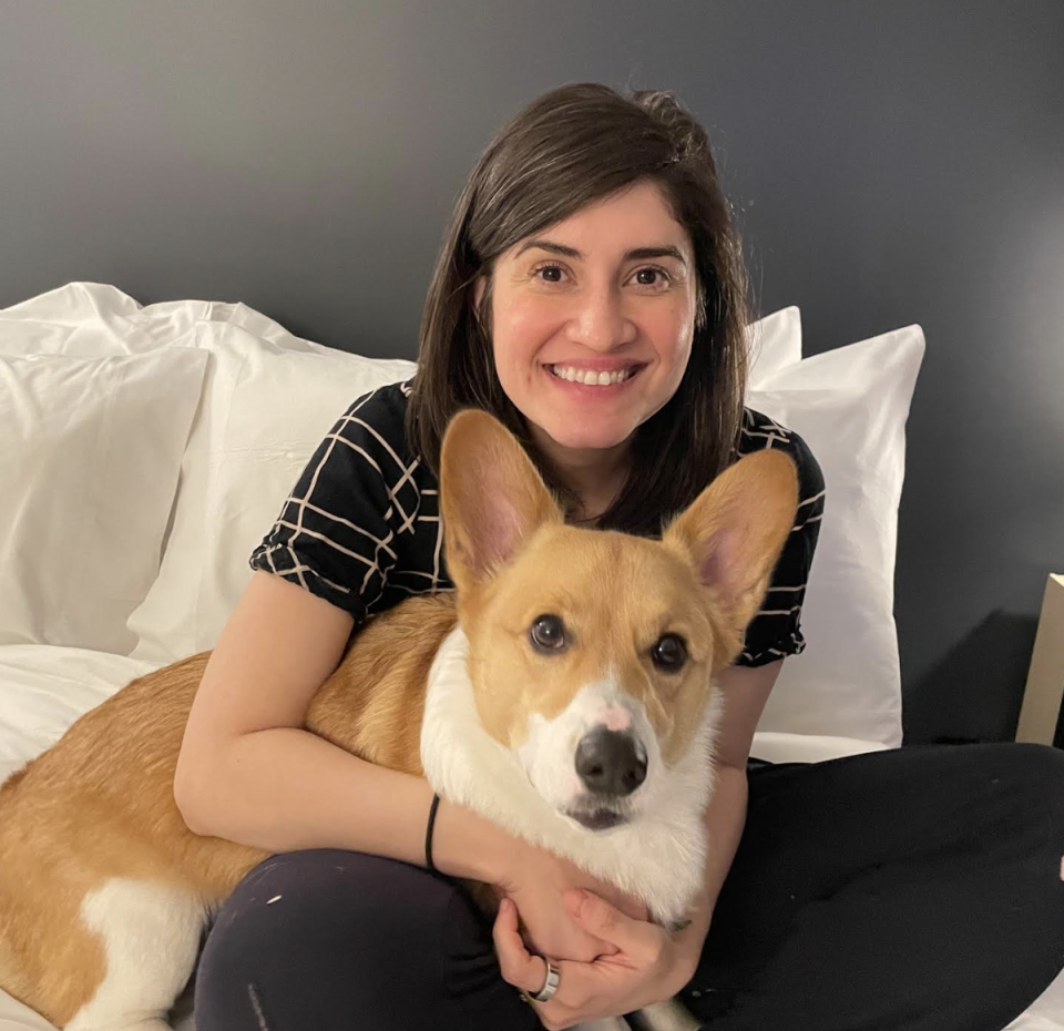 Woman smiling, sitting on a bed with a Corgi, in a cozy hotel room setting