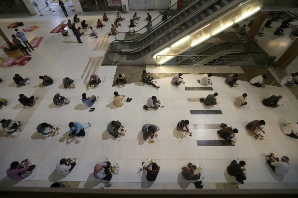 FILE- In this April 7, 2020 file photo, migrant workers from other states and the homeless eat dinner at a shelter set up at a mall during lockdown to prevent the spread of new coronavirus in Ahmedabad, India. India, a bustling country of 1.3 billion people, has slowed to an uncharacteristic crawl, transforming ordinary scenes of daily life into a surreal landscape. The country is now under what has been described as the world’s biggest lockdown, aimed at keeping the coronavirus from spreading and overwhelming the country’s enfeebled health care system. (AP Photo/Ajit Solanki, File)