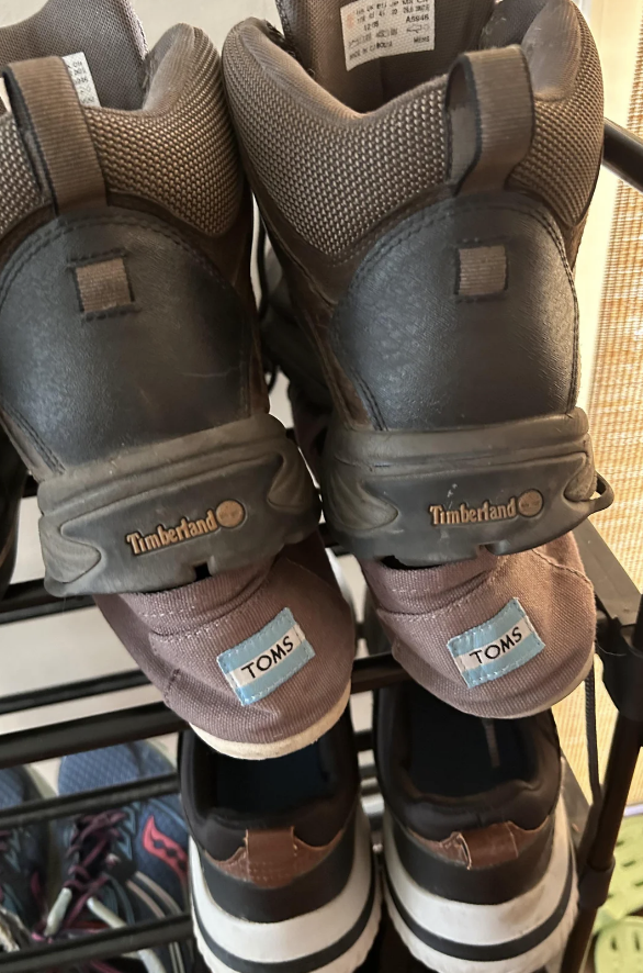 Two Timberland-branded boots with straps on a rack. They feature TOMS patches