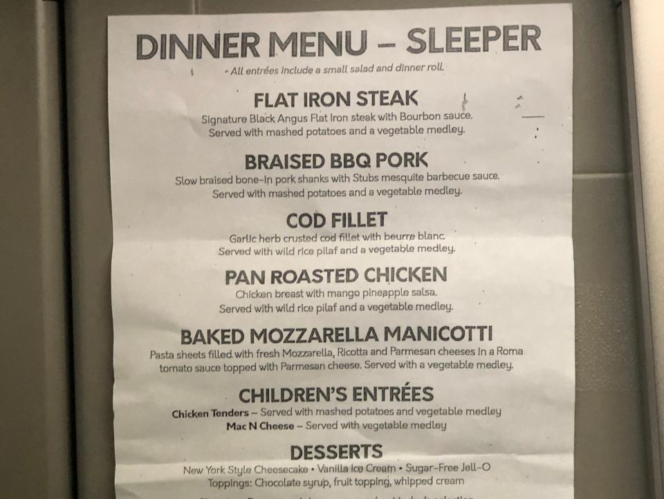 Amtrak dinner menu on sheet of white paper with flat iron steak, bbq pork, and other options printed on it with amtrak logo on the bottom