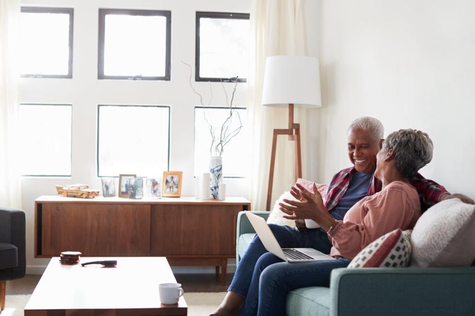 Two people sitting on a couch smiling and looking at a laptop.