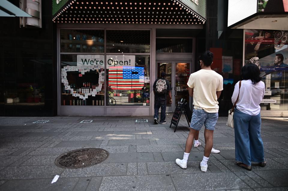 The American flag is reflected in a Cafe as people queue for coffee at Times Square as New York City enters phase two of reopening June 22, 2020. - New York City begins phase two reopening on June 22, 2020 as people can eat outdoors at restaurants and barbershops and salons can also open at 50 percent capacity. (Photo by Johannes EISELE / AFP) (Photo by JOHANNES EISELE/AFP via Getty Images)