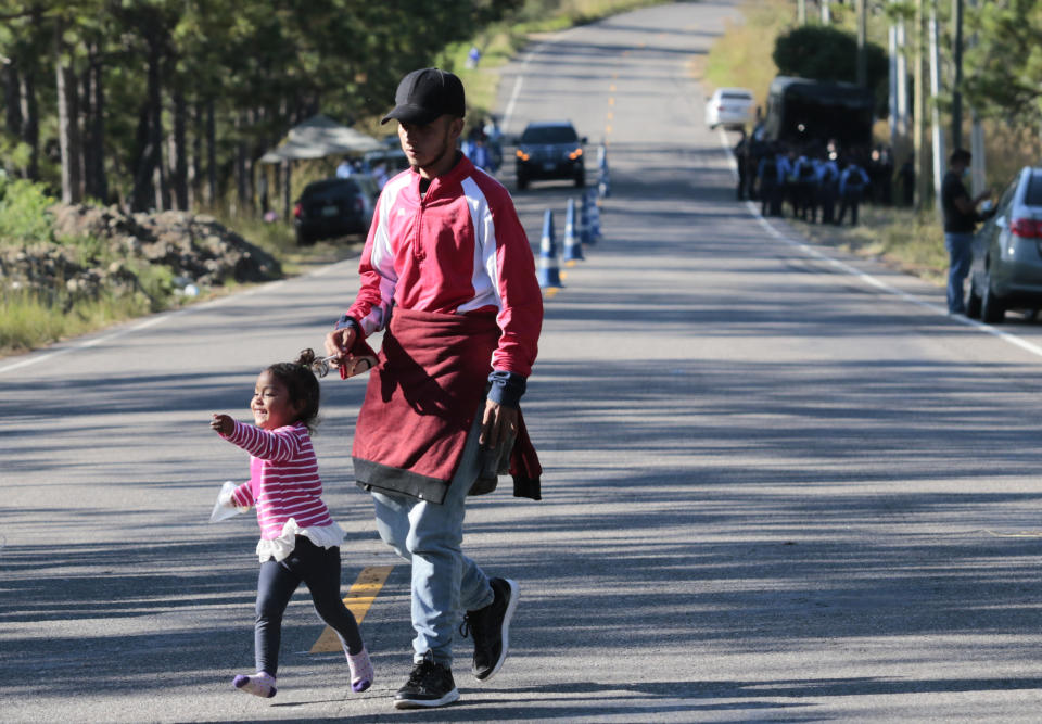 A migrant and his daughter walk near a police checkpoint on their way North near Agua Caliente, close to the border with Guatemala, Thursday, Dec. 10, 2020. Honduran security forces stationed on the highway a few kilometers before Agua Caliente, asked the migrants for their passports or identity cards and proof of a COVID-19 test, and if they did not produce those documents they would not be allowed to move on. (AP Photo/Delmer Martinez)