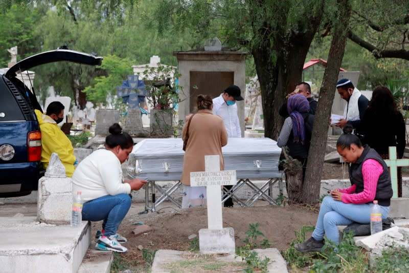 A funeral worker looks at a family saying their last goodbyes to their relative who died of the coronavirus disease (COVID-19) at the San Lorenzo Tezonco cemetery in Mexico City
