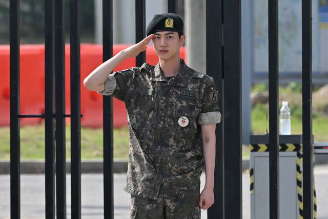 <p>JUNG YEON-JE/AFP via Getty</p> Jin salutes after being discharged from his mandatory military service in front of a military base in South Korea on June 12