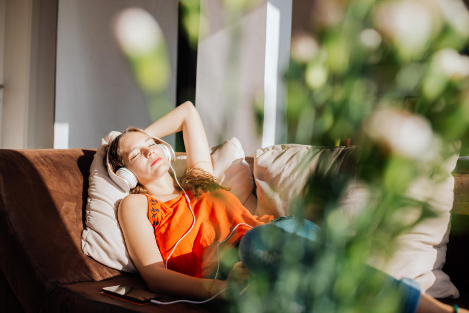 Woman relaxing on a couch with headphones, eyes closed, surrounded by indoor plants