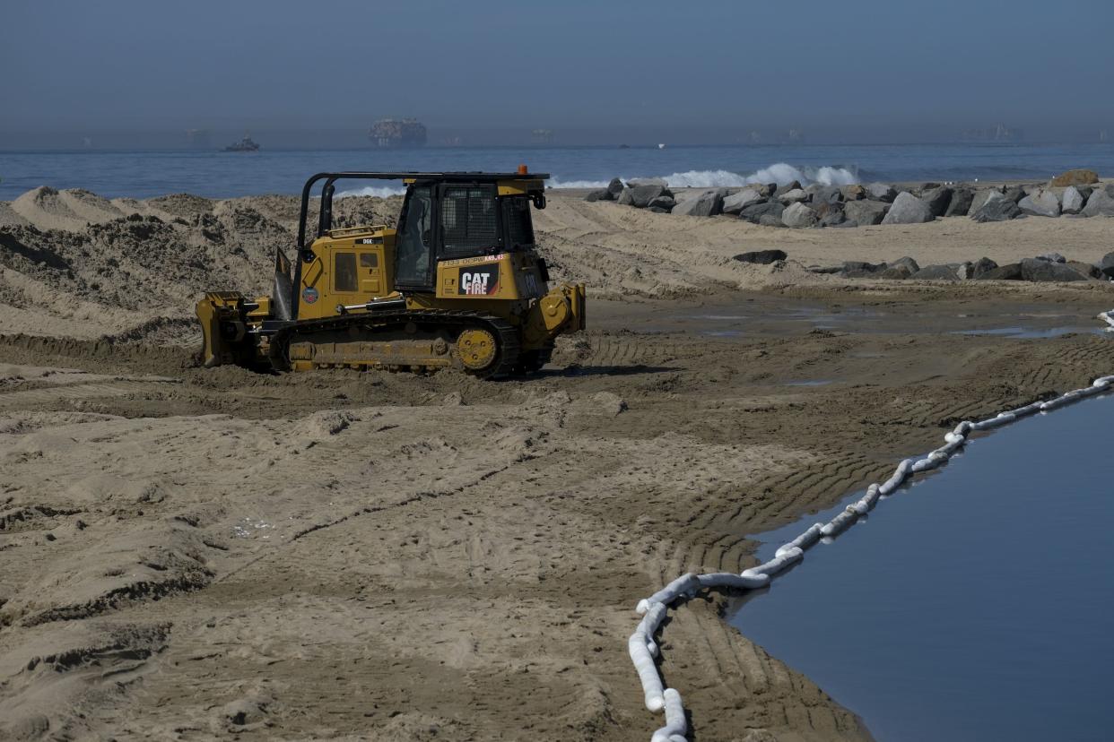 Heavy machinery is used to build sand barriers to contain oil washed up in Huntington Beach, Calif., Sunday, Oct. 3, 2021.