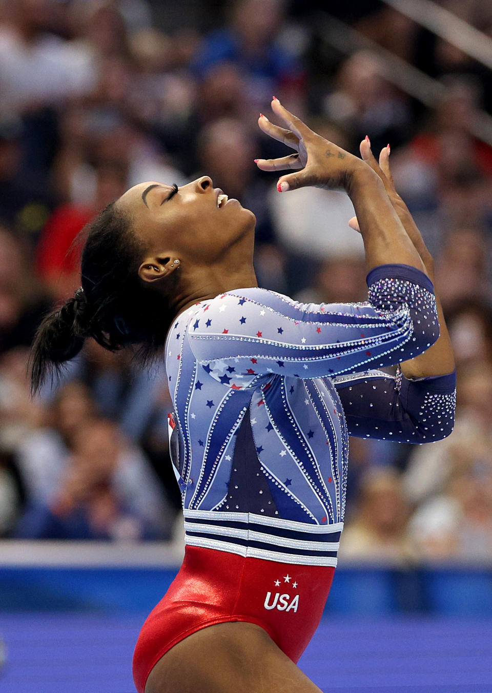 Simone Biles performing a rhythmic pose in a USA leotard at a gymnastics event