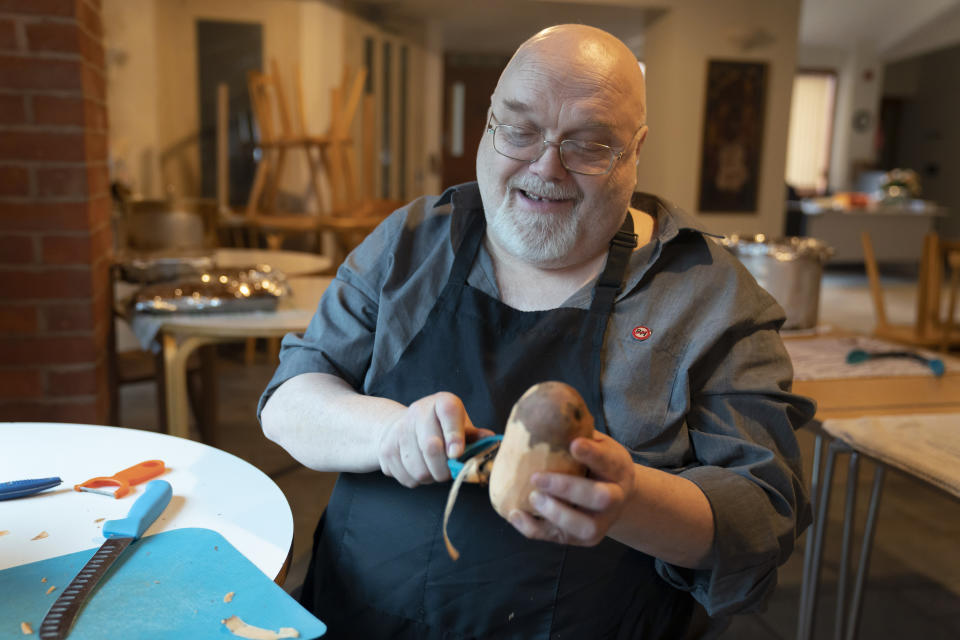 Volunteer Ian Cash peels a sweet pototao, as members the Preston Windrush Covid Response team prepare West Indian meals, at the Xaverian Sanctuary, in Preston, England, Friday Feb. 19, 2021. Once a week, chief coordinator Glenda Andrew and her team distribute meals to people in Preston and surrounding communities in northwestern England that have recorded some of the U.K.’s highest coronavirus infection rates. The meal program grew out of Andrew’s work with Preston Windrush Generation & Descendants, a group organized to fight for the rights of early immigrants from the Caribbean and other former British colonies who found themselves threatened with deportation in recent years. (AP Photo/Jon Super)