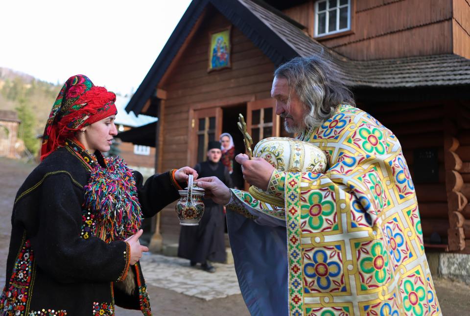 A priest blesses water for a woman as local residents dressed in national costumes celebrate Epiphany in Kryvorivnya village in the Carpathian Mountains near Ivano-Frankivsk, western Ukraine, 06 January 2023 (EPA)