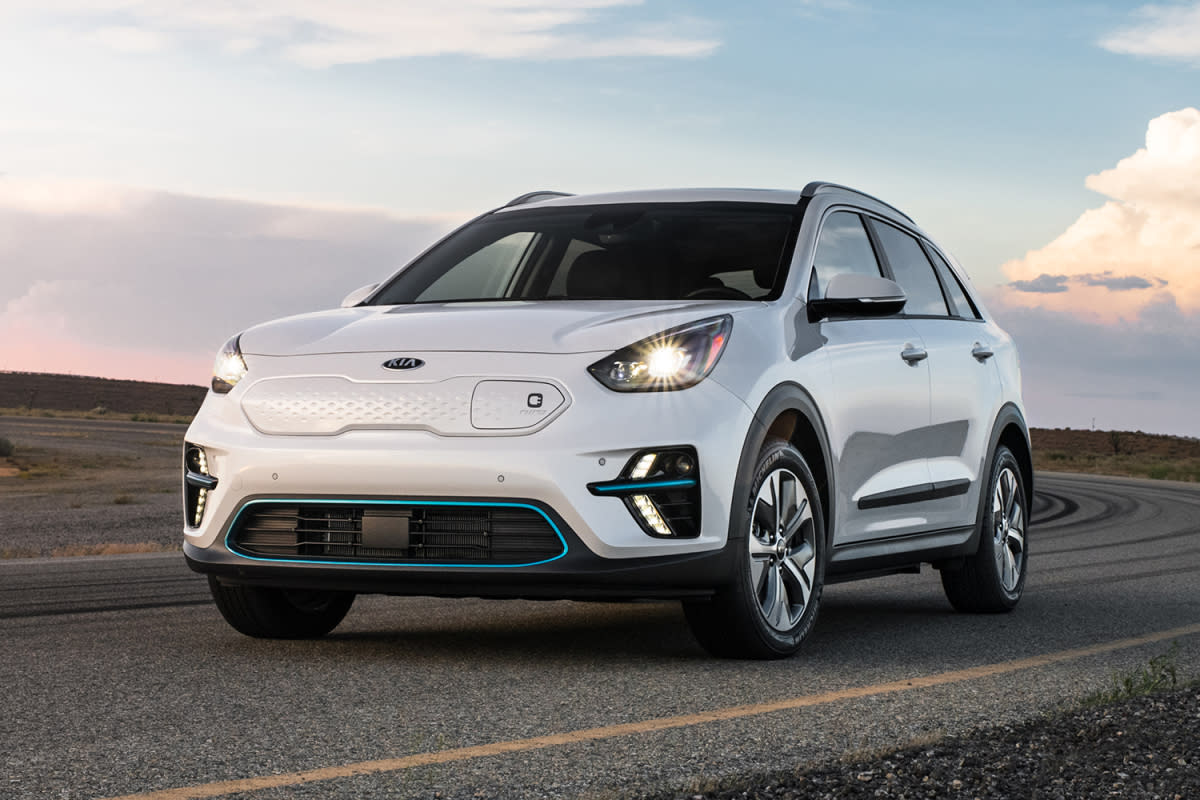 A white Kia Niro EV driving down a remote road during sunset