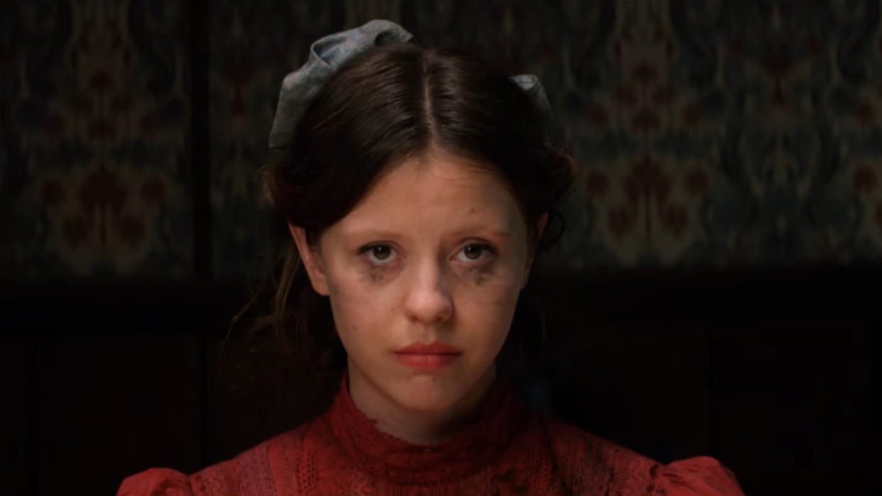  Mia Goth stares straight ahead with smudged makeup at the dinner table in Pearl. 