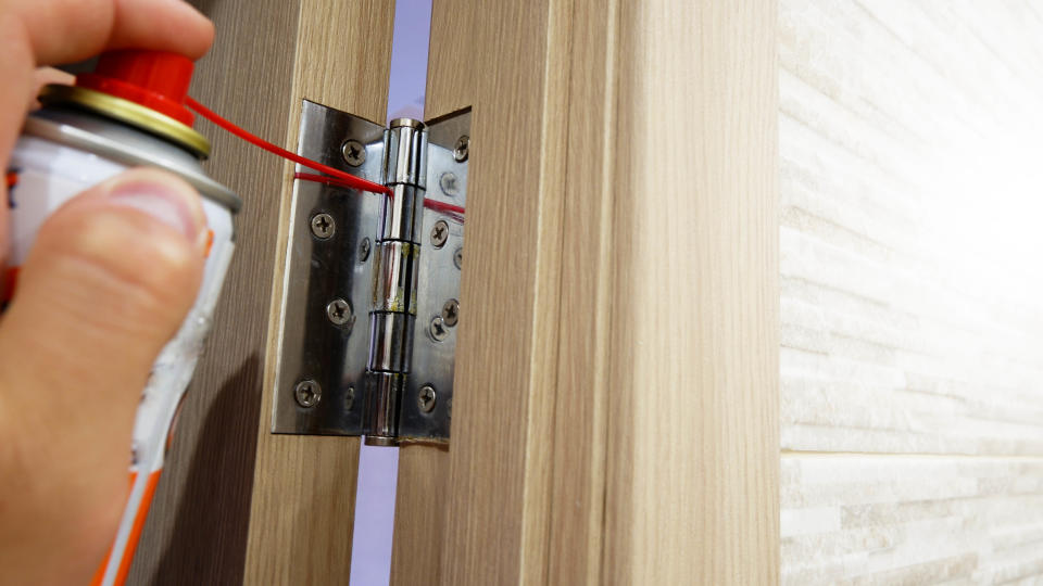 A lubricant being sprayed on a door hinge