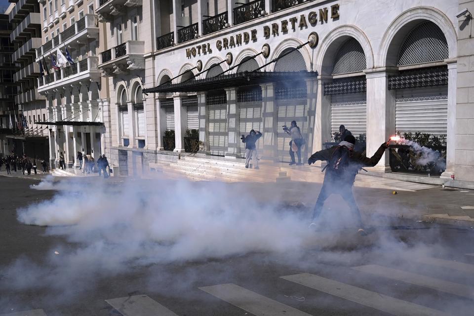 A demonstrator throws a flare to riot police during clashes in Athens, Greece, Sunday, March 5, 2023. Thousands protesters, take part in rallies around the country for fifth day, protesting the conditions that led the deaths of dozens of people late Tuesday, in Greece's worst recorded rail accident. (AP Photo/Aggelos Barai)