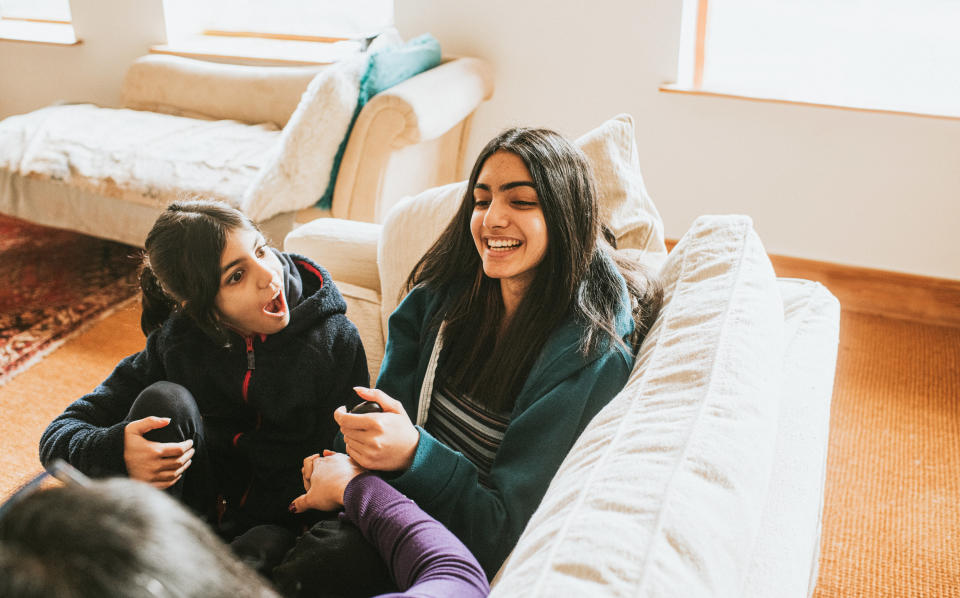 Teenage daughter and her little sister sit with their feet up on a cream sofa, while their Mum looks over at them