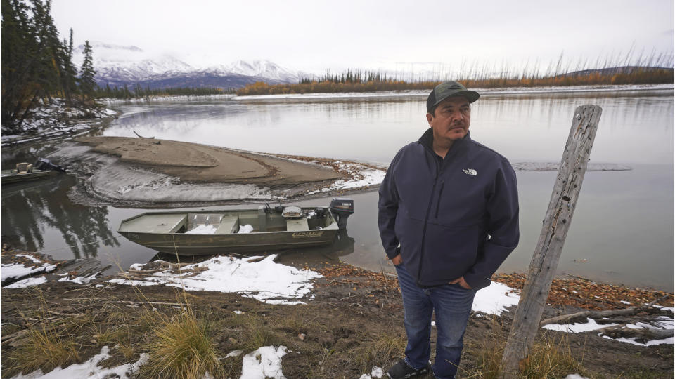 Herbie Demit, Tanacross Village Council president, looks on as boat sits near a landing Thursday, Sept. 23, 2021, in Tanacross, Alaska. Behind the boat is the Tanana River, which flows in front of the Alaska Range. Alaska is experiencing one of the sharpest rises in COVID-19 cases in the country, coupled with a limited statewide healthcare system that is almost entirely reliant on Anchorage hospitals. (AP Photo/Rick Bowmer)