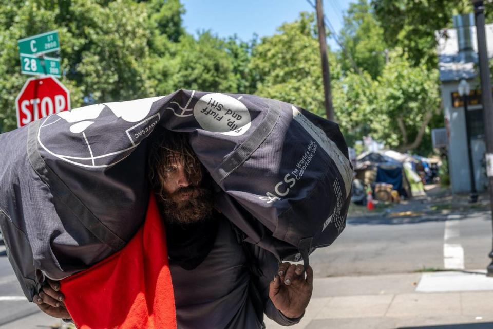 Homeless camper Chadwick Justin Foy, 41, right, holds all his belongings on his shoulders as he relocates from the intersection of 28th and C streets on Tuesday, July 18, 2023. The city has given notices to dozens of people living in tents on the sidewalks in that area, near Leland Stanford Park, telling them to move by Wednesday. The notices cite violation of city codes regarding sidewalk obstruction and storage of personal property on public property.