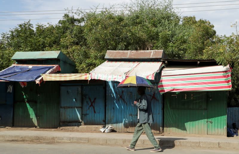 A man holds an umbrella as he walks past closed shops in Sanja, Amhara region near a border with Tigray