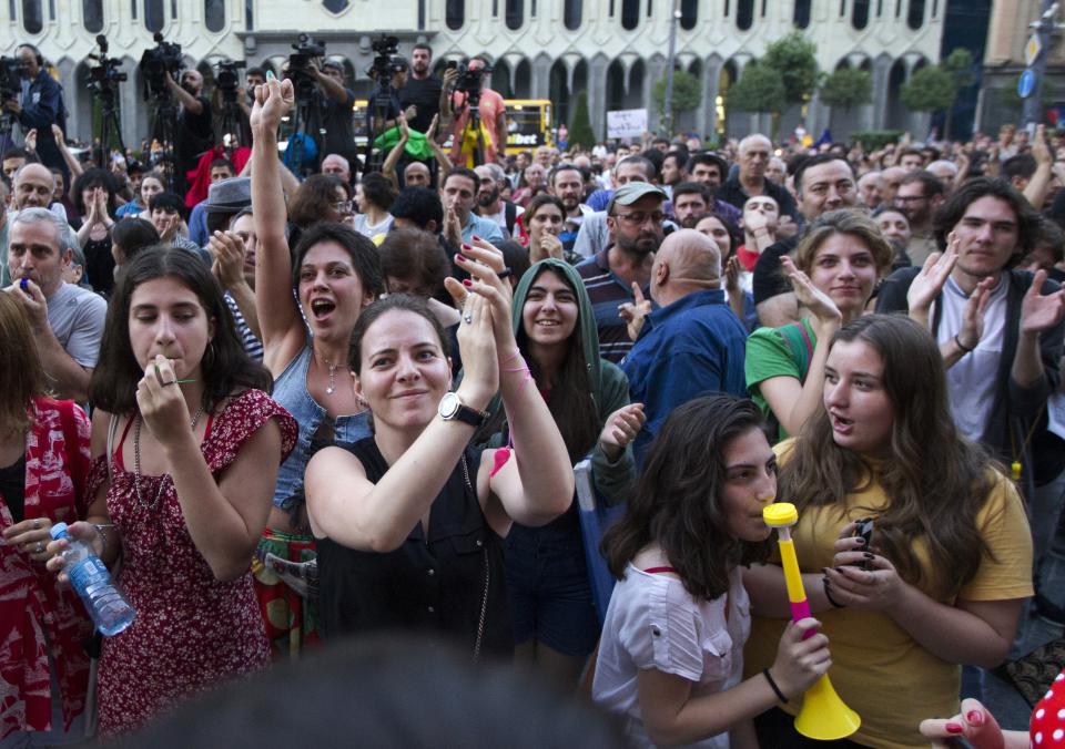 People applaud and listen to a speaker during a protest as opposition demonstrators gather in front of the Georgian Parliament building in Tbilisi, Georgia, Monday, June 24, 2019. Demonstrators have returned to parliament for daily rallies, demanding the release of detained protesters, the ouster of the nation's interior minister and changes in the electoral law to have legislators chosen fully proportionally rather than the current mix of party-list and single-mandate representatives. (AP Photo/Shakh Aivazov)