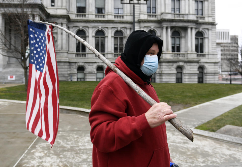 A man representing a group called "The American People" walks with a flag during a protest rally for President Donald Trump ahead of the inauguration of President-elect Joe Biden and Vice President-elect Kamala Harris at the New York State Capitol Sunday, Jan. 17, 2021, in Albany, N.Y. (AP Photo/Hans Pennink)