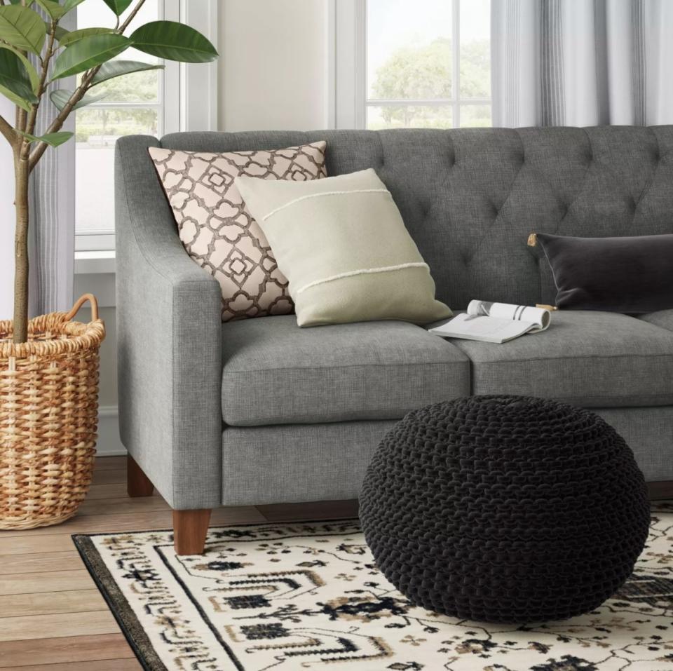 The chunky knit pouf in black sitting in front of a gray tufted sofa